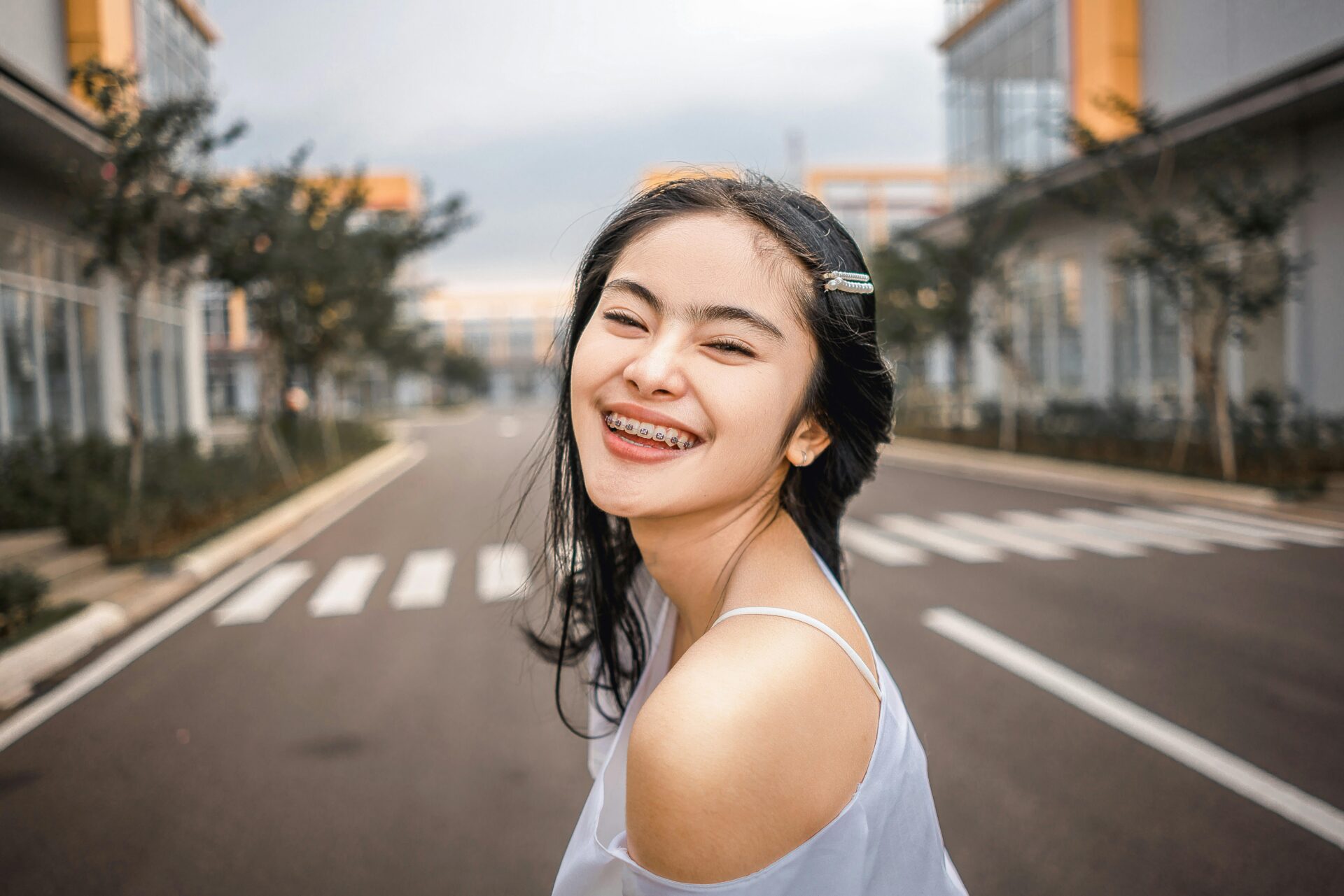 Young lady pauses and smiles for the camera in the middle of the street, showing off braces.