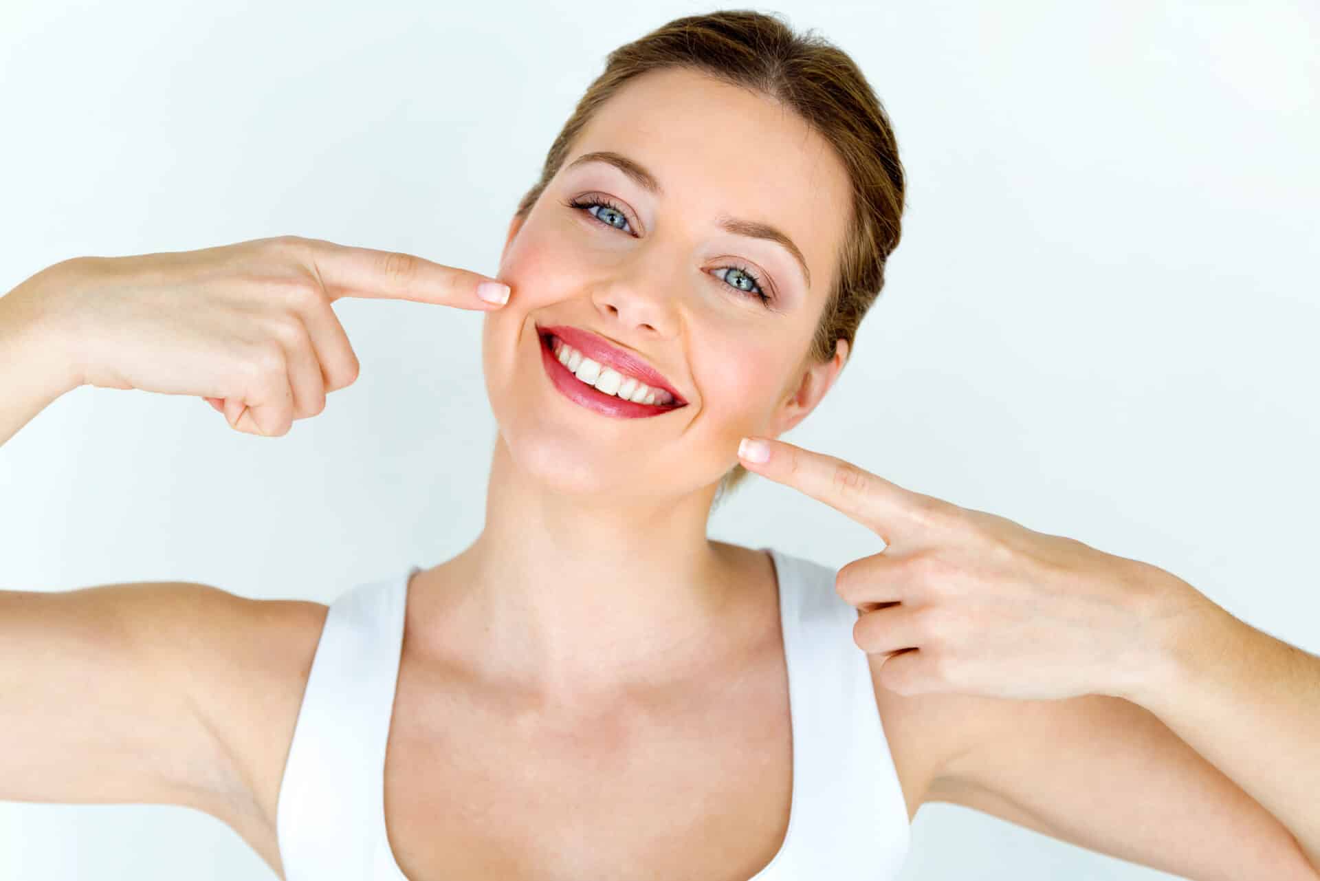 Brown-haired woman points with both hands to perfect smile from great dental care.