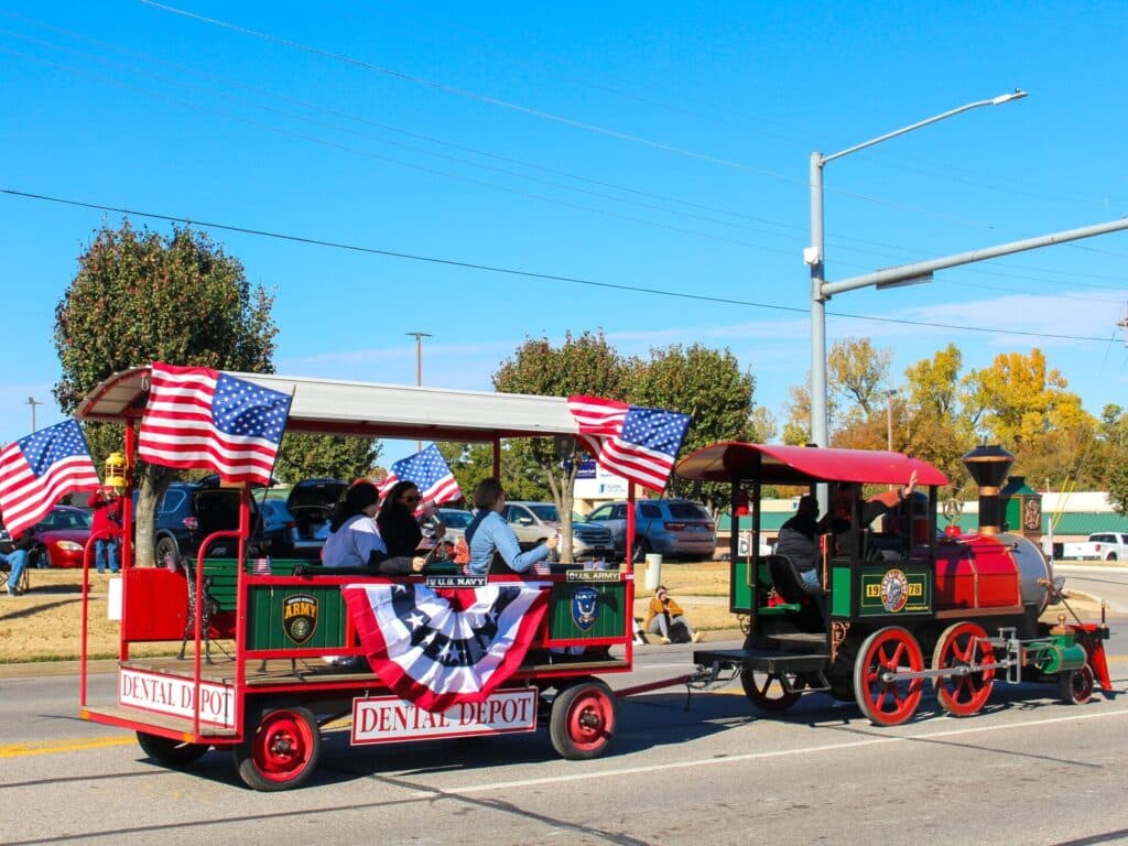 A Dental Depot branded model train drives down the road in a parade.