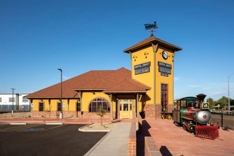 Exterior view of Surprise dentist office with yellow exterior, model train, and clock tower