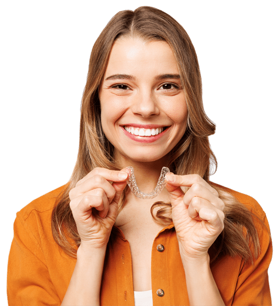 A woman smiles at the camera while holding Invisalign aligners in the shape of a heart.