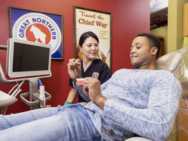 A man looks at Invisalign models while sitting in the dental chair.