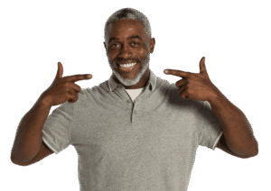Man smiling from perfect dental implants while standing against white background in a grey shirt.