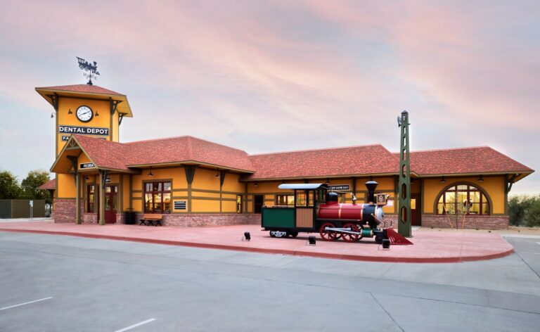 Exterior view of the Peoria, AZ dental clinic with yellow walls, a red roof, a clock, and a large train model.